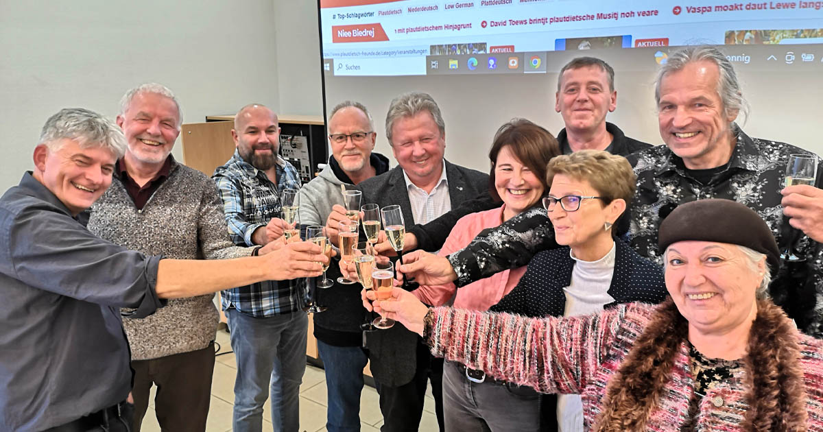 Daut Bild wiest, woo mehrere Mensche met Sekt aunsteete. Dee Grund ess daut 25-joahsche Jubileum vom Verein Plautdietsch-Freunde.